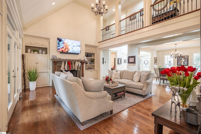 living room featuring hardwood / wood-style floors, crown molding, a high ceiling, built in shelves, and a chandelier