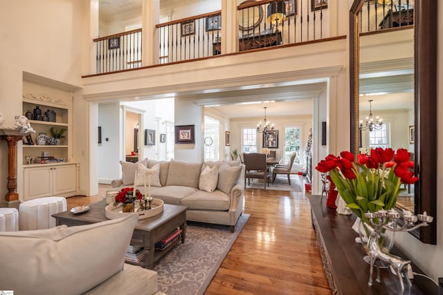 living room with wood-type flooring, a towering ceiling, an inviting chandelier, and ornamental molding