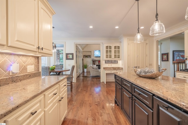 kitchen with decorative light fixtures, crown molding, dark brown cabinetry, and light stone countertops