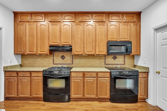 kitchen with black appliances, exhaust hood, light stone counters, and tasteful backsplash