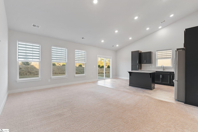 unfurnished living room with sink, light colored carpet, and lofted ceiling