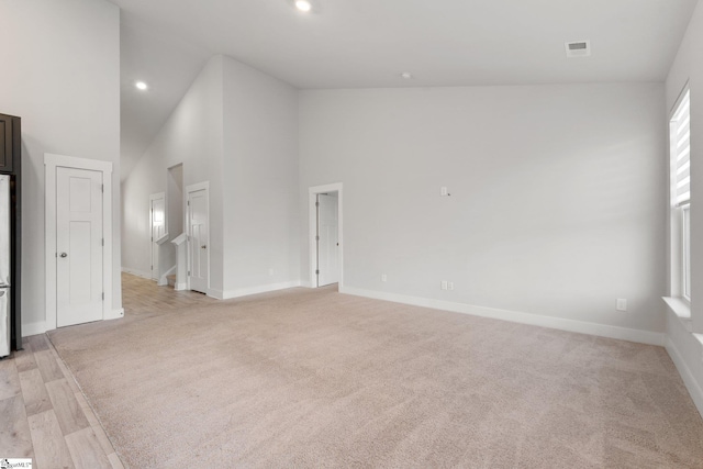 empty room with high vaulted ceiling and light hardwood / wood-style flooring