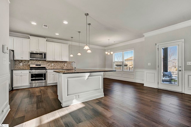 kitchen featuring white cabinets, decorative light fixtures, stainless steel appliances, a center island with sink, and crown molding