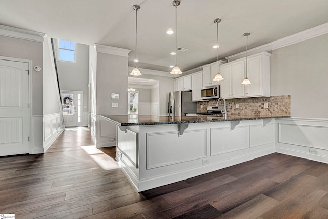 kitchen with white cabinets, decorative light fixtures, stainless steel appliances, dark stone countertops, and kitchen peninsula