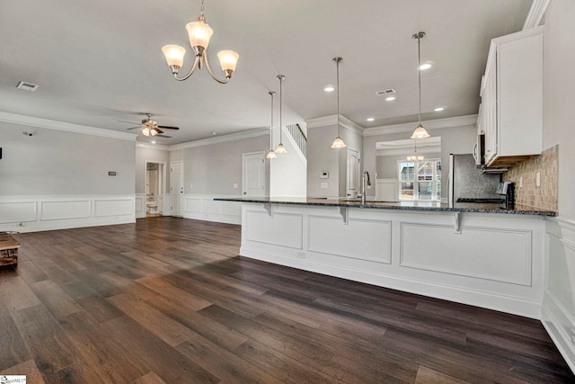 kitchen with white cabinetry, kitchen peninsula, decorative light fixtures, dark stone countertops, and sink