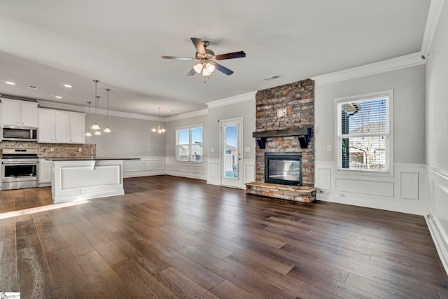 unfurnished living room featuring a fireplace, ceiling fan with notable chandelier, ornamental molding, and dark hardwood / wood-style floors