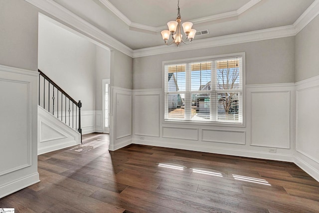 unfurnished dining area with dark wood-type flooring, a tray ceiling, crown molding, and a notable chandelier