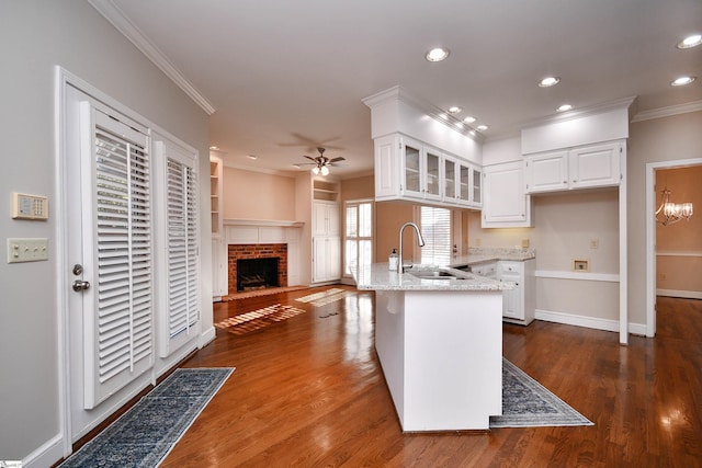 kitchen featuring white cabinetry, a brick fireplace, dark wood-type flooring, light stone counters, and sink