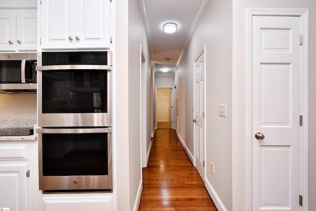 kitchen featuring hardwood / wood-style floors, white cabinets, stainless steel appliances, light stone counters, and crown molding