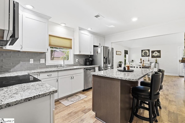 kitchen featuring a kitchen island, sink, white cabinetry, light stone countertops, and appliances with stainless steel finishes