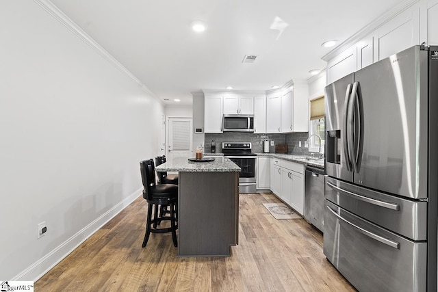 kitchen featuring light stone counters, white cabinets, a center island, and stainless steel appliances