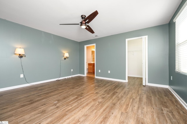 unfurnished bedroom with ceiling fan, a closet, a spacious closet, and light wood-type flooring