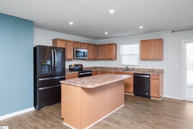 kitchen with black appliances, a kitchen island, light hardwood / wood-style floors, sink, and a kitchen breakfast bar