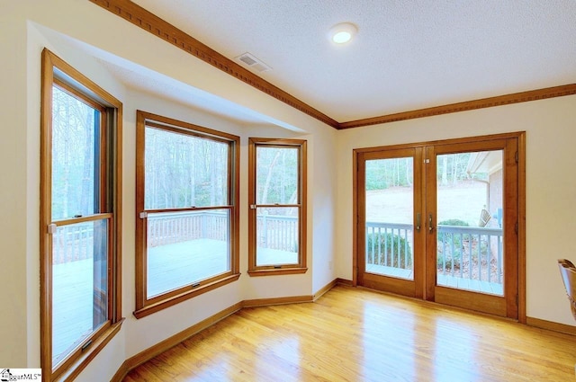 empty room with a healthy amount of sunlight, crown molding, a textured ceiling, and light hardwood / wood-style floors