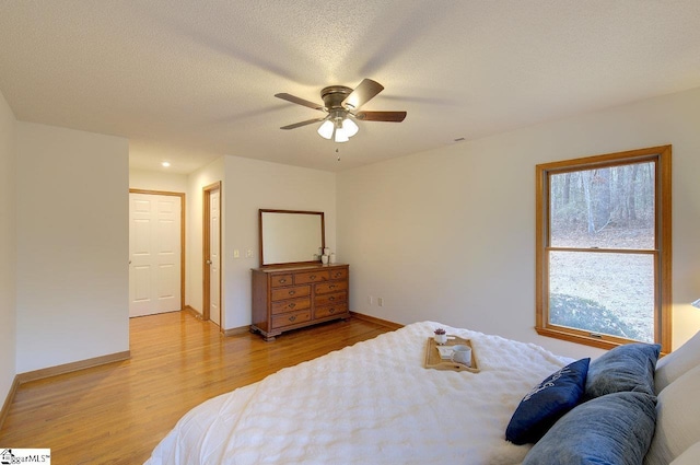 bedroom featuring a textured ceiling, ceiling fan, light hardwood / wood-style flooring, and multiple windows