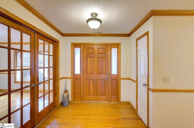 foyer entrance with a textured ceiling, ornamental molding, light hardwood / wood-style flooring, and french doors