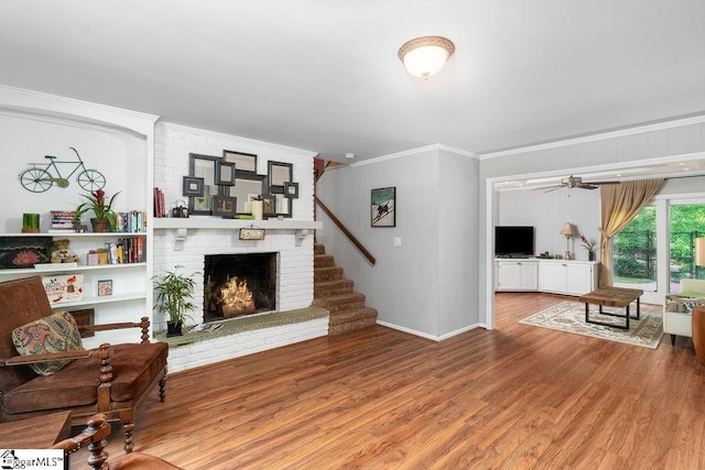 living room featuring ceiling fan, a brick fireplace, crown molding, and hardwood / wood-style floors