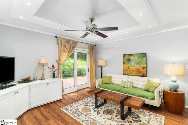 living room featuring a raised ceiling, light wood-type flooring, and crown molding