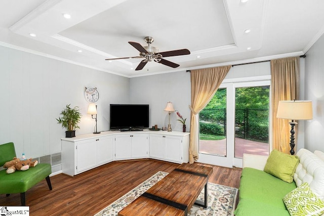 living room with ceiling fan, dark wood-type flooring, a tray ceiling, and ornamental molding