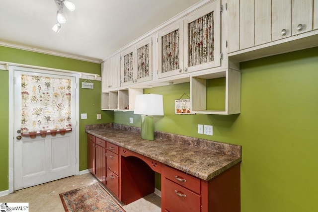 kitchen with stone counters, light tile patterned floors, ornamental molding, and built in desk