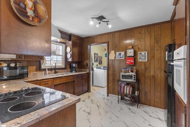 kitchen featuring washer / clothes dryer, sink, wooden walls, white oven, and black electric cooktop