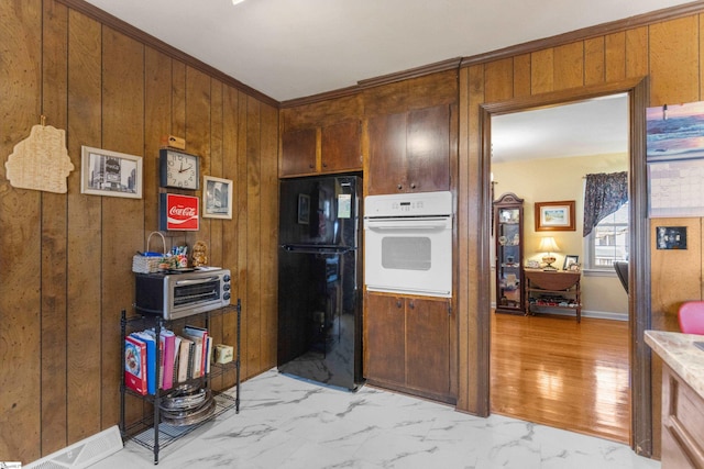 kitchen with white oven, crown molding, wood walls, and black refrigerator