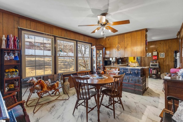 dining space featuring ceiling fan, a healthy amount of sunlight, and wooden walls