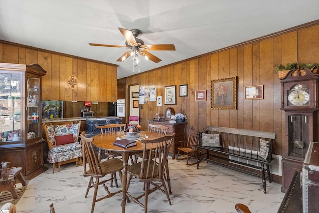 dining room featuring ceiling fan, ornamental molding, and wooden walls