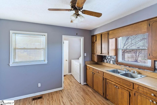 kitchen with washer / dryer, ceiling fan, tasteful backsplash, light wood-type flooring, and sink