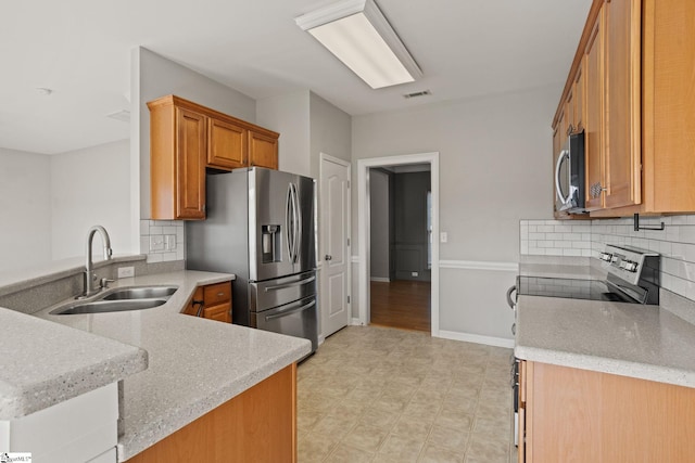 kitchen with kitchen peninsula, appliances with stainless steel finishes, tasteful backsplash, light stone countertops, and sink