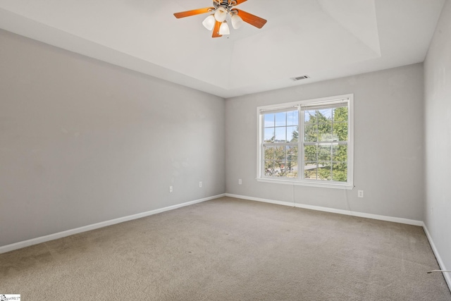 carpeted empty room featuring ceiling fan and a raised ceiling