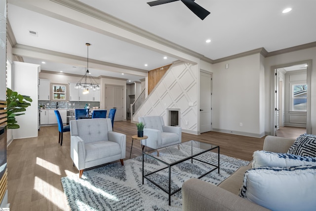 living room with a wealth of natural light, ceiling fan with notable chandelier, ornamental molding, and light hardwood / wood-style flooring