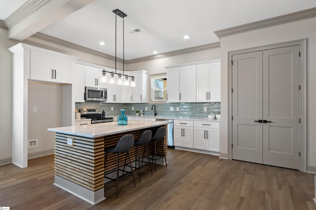 kitchen featuring appliances with stainless steel finishes, white cabinets, decorative light fixtures, and a center island