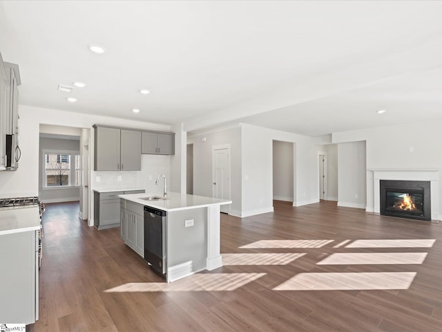 kitchen featuring appliances with stainless steel finishes, open floor plan, a kitchen island with sink, gray cabinetry, and a sink