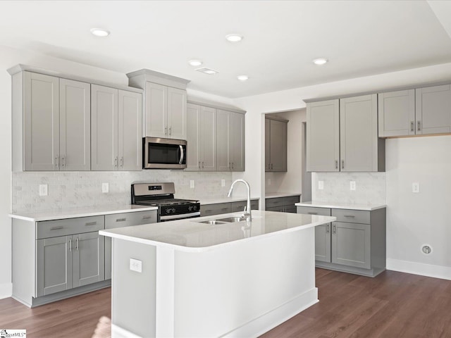 kitchen with gray cabinetry, a sink, appliances with stainless steel finishes, dark wood finished floors, and a center island with sink