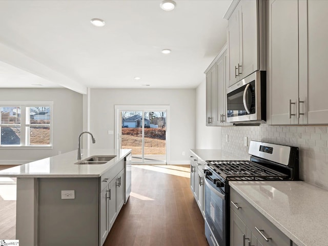 kitchen with dark wood-style flooring, stainless steel appliances, gray cabinets, backsplash, and a sink