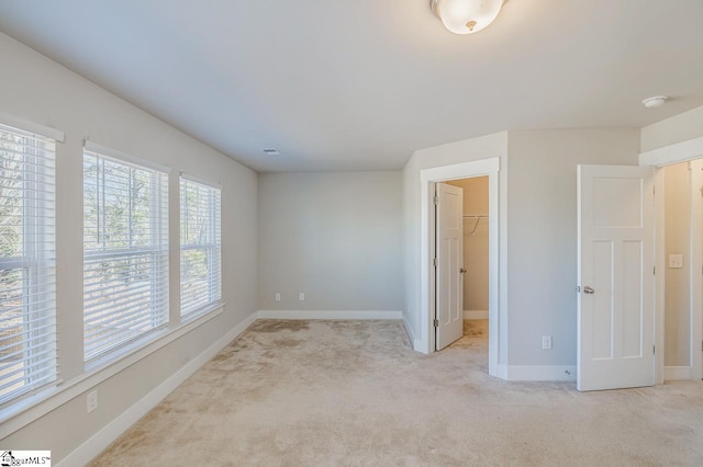 unfurnished bedroom with a walk in closet, a closet, and light colored carpet