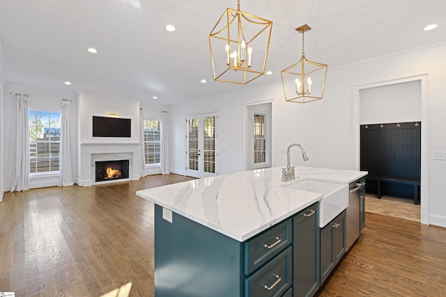 kitchen featuring light stone countertops, pendant lighting, a high end fireplace, sink, and a center island with sink