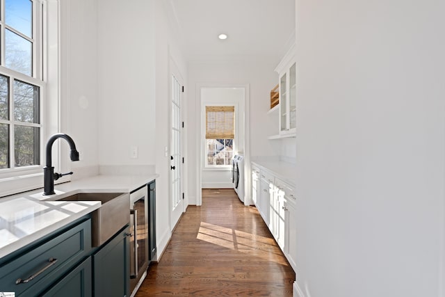 kitchen with beverage cooler, white cabinets, washer / dryer, dark wood-type flooring, and sink