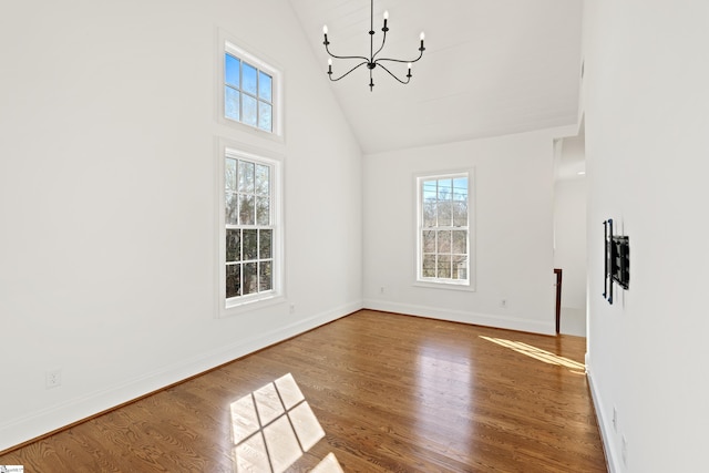 unfurnished living room with a chandelier, a healthy amount of sunlight, hardwood / wood-style flooring, and high vaulted ceiling