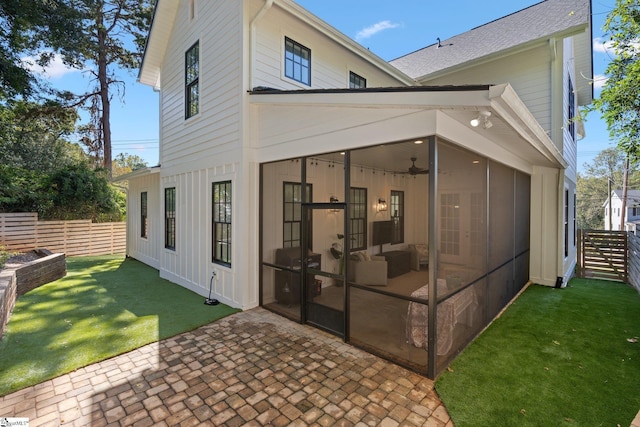 rear view of property featuring ceiling fan, a patio area, a sunroom, and a lawn