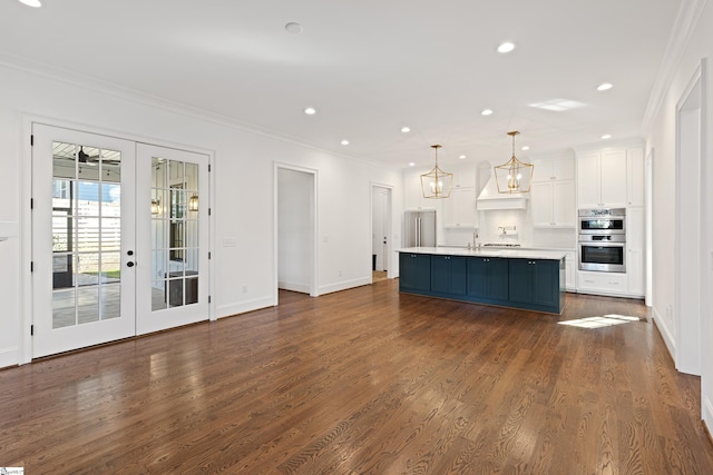 kitchen featuring appliances with stainless steel finishes, white cabinetry, french doors, an island with sink, and hanging light fixtures