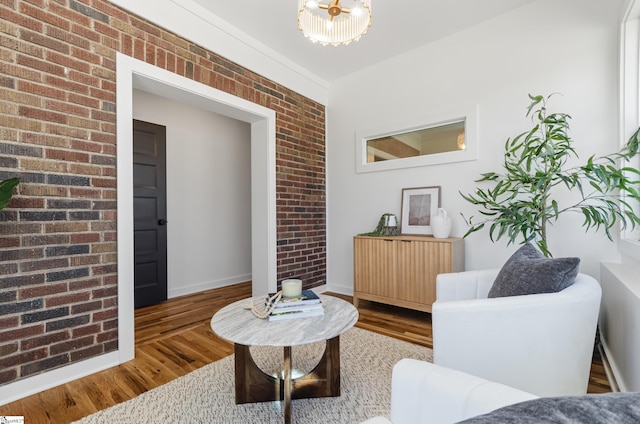sitting room featuring hardwood / wood-style flooring, brick wall, and a chandelier