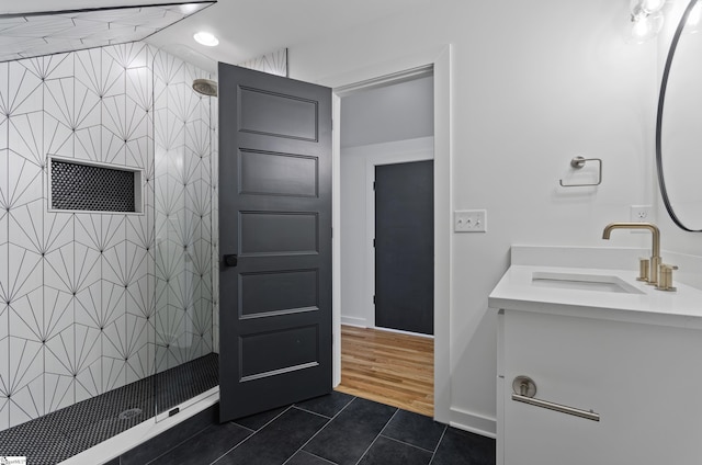 bathroom with tile patterned flooring, a tile shower, and vanity