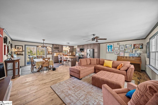 living room with light hardwood / wood-style floors, crown molding, and ceiling fan with notable chandelier