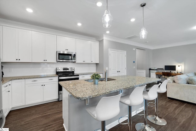 kitchen with white cabinets, stainless steel appliances, hanging light fixtures, a center island with sink, and a breakfast bar area