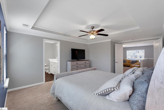 bedroom with ceiling fan, a tray ceiling, ornamental molding, and ensuite bathroom