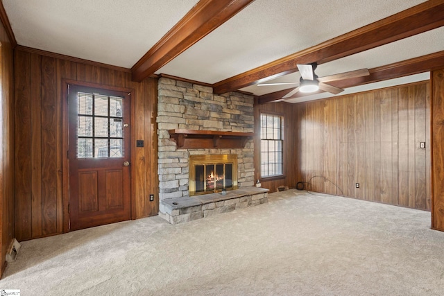 unfurnished living room featuring a textured ceiling, a stone fireplace, beamed ceiling, wooden walls, and carpet flooring