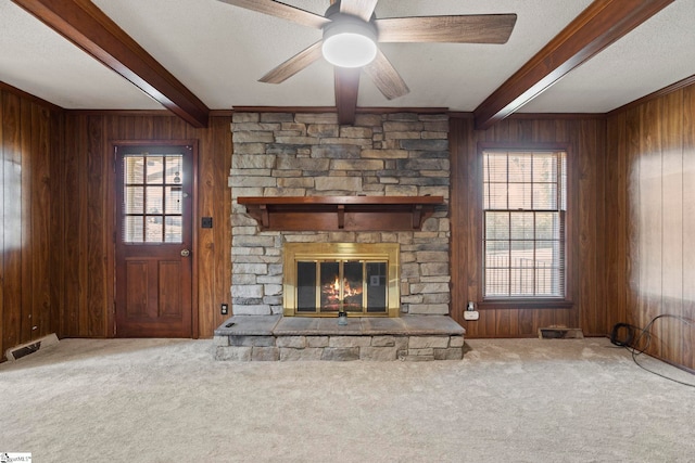 unfurnished living room with beam ceiling, plenty of natural light, carpet, and wood walls