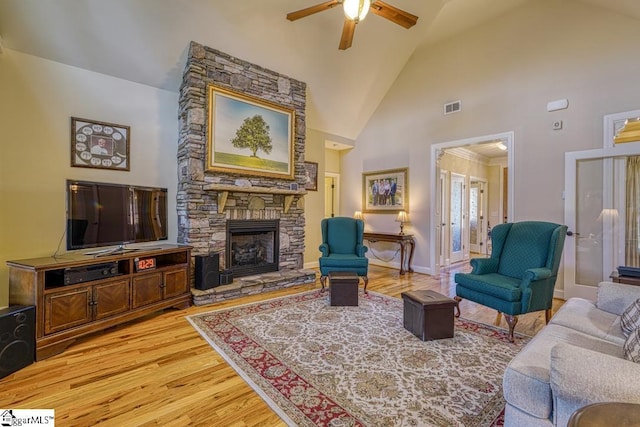 living room featuring light wood-type flooring, ceiling fan, a stone fireplace, and high vaulted ceiling